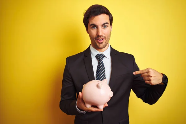 Young Handsome Businessman Holding Piggy Bank Isolated Yellow Background Surprise — Stock Photo, Image