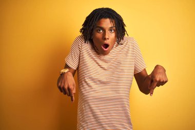 Çizgili t-shirt giyen dreadlocks giyen Afro adam izole sarı arka plan reklam gösteren parmakları ile aşağı işaret, sürpriz yüz ve açık ağız