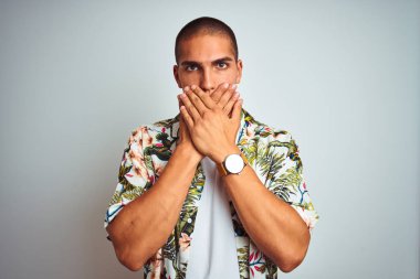 Tatilde beyaz arka plan üzerinde Hawaii gömlek giyen genç yakışıklı adam hata için elleri ile ağız kapsayan şok. Gizli kavram.