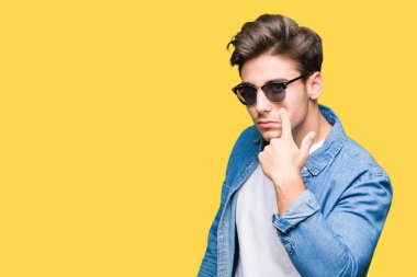 Genç yakışıklı adam giyen güneş gözlüğü izole üzerinde arka plan işaret jest göz izlemek için şüpheli ifade