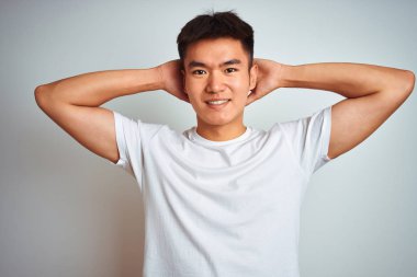 Genç asya çinli adam izole beyaz arka plan üzerinde duran t-shirt giyen rahatlatıcı ve germe, kollar ve eller baş ve boyun arkasında mutlu gülümseyerek