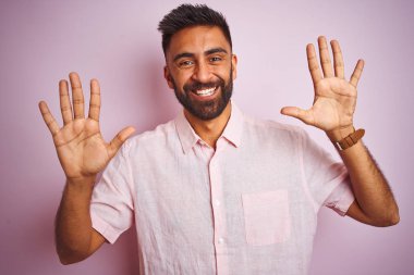 Genç hintli adam izole pembe arka plan üzerinde duran rahat gömlek giyen gösteren ve emin ve mutlu gülümserken parmakları on numara ile işaret.