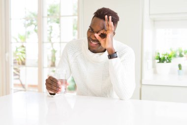 Afro-amerikan adam mutlu yüz ile su taze bir bardak driking parmakları ile bakarak göz eliyle ok işareti yapıyor gülümseyerek