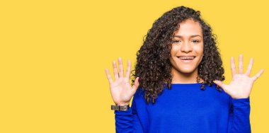 Gösterilen ve parmakları ile işaret kıvırcık saçlı giyen kış kazaklı genç güzel kadın kendinden emin ve mutlu gülümseyerek süre on numara.