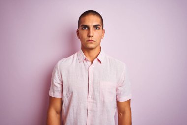 Genç yakışıklı adam yüzünde ciddi bir ifade ile pembe izole arka plan üzerinde zarif gömlek giyiyor. Kameraya basit ve doğal bir bakış.