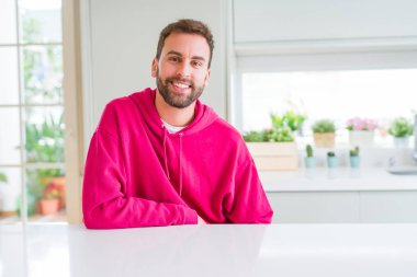 Evde rahat sweatshirt giyen ve olumlu gülümseyen yakışıklı adam