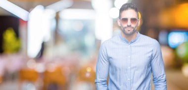 Genç yakışıklı adam yüzünde ciddi bir ifade ile izole arka plan üzerinde güneş gözlüğü takıyor. Basit ve doğal kameraya bakıyor.