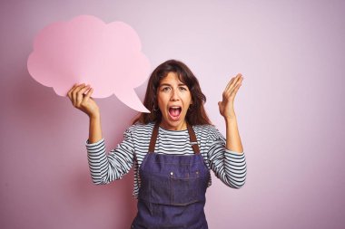 Izole pembe arka plan üzerinde bulut konuşma balonu tutan önlük giyen güzel şef kadın çok mutlu ve heyecanlı, kazanan ifade büyük bir gülümseme ile çığlık zafer kutluyor ve ellerini kaldırdı