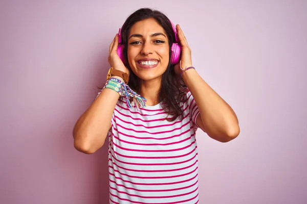 顔に幸せでクールな笑顔で孤立したピンクの背景の上にヘッドフォンを使用して音楽を聴く若い美しい女性 ラッキーな人 — ストック写真