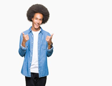 El ile pozitif jest yapıyor afro saçlar başarı işareti ile genç Afro-Amerikan adam başparmak gülümseyen ve mutlu. Neşeli bir ifadeyle, kazanan jest kameraya bakıyor.