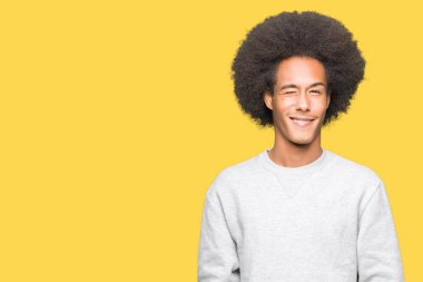 Afro saçlı seksi bir ifadeyle, neşeli ve mutlu yüzünü kameraya bakarak sportif kazak göz kırpıyor giyen genç Afro-Amerikan adam.