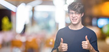 Yakışıklı delikanlı izole arka plan başarı işareti el ile pozitif jest yapıyor üzerinde gözlük takan başparmak gülümseyen ve mutlu. Neşeli bir ifadeyle, kazanan jest kameraya bakıyor.