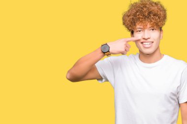 Neşeli gülümseyen casual beyaz t-shirt işaretçi el parmak yüz ve burun, giyen afro saçlı Genç yakışıklı adam