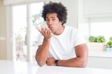 Genç afro-amerikan adam rahat beyaz t-shirt giyen evde oturan kamera hava güzel ve seksi olmak eliyle bir öpücük üfleme bakarak. Aşk ifadesi.
