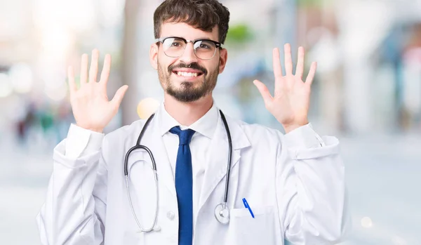 年轻的医生男子穿着医院外套在孤立的背景显示和手指指向数字十 同时微笑着自信和快乐 — 图库照片