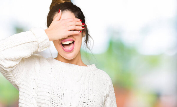 Young beautiful woman wearing winter sweater smiling and laughing with hand on face covering eyes for surprise. Blind concept.