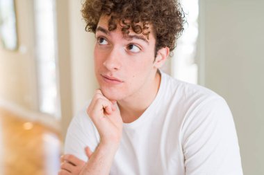 Genç yakışıklı giyen beyaz t-shirt çene düşünme hakkında soru, dalgın ifade üzerine el ile adam. Düşünceli yüzüyle gülümsüyor. Şüphe kavramı.