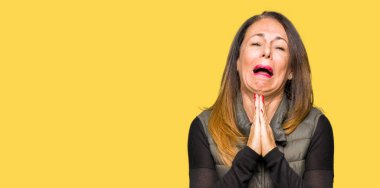 Kış yelek yalvarıyor ve umut ifade yüzünde çok duygusal ve endişe ile birlikte elleriyle dua giyen güzel orta yaş kadın. Bağışlanmak. Din kavramı.