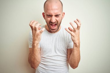 Sakallı genç kel adam izole arka plan üzerinde rahat beyaz t-shirt giyen silah kaldırdı ve kapalı gözleri heyecanlı çığlık ile başarı için deli ve deli kutluyor. Kazanan kavramı