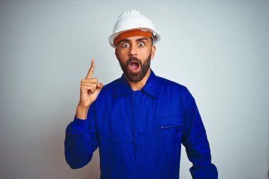 Yakışıklı hintli işçi adam izole beyaz arka plan üzerinde üniforma ve kask giyen başarılı bir fikir ile parmak işaret. Çıktı ve mutlu. Bir numara.