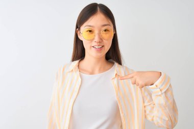 Kendine parmak işaret sürpriz yüzü ile izole beyaz arka plan üzerinde çizgili gömlek ve gözlük giyen genç Çinli kadın