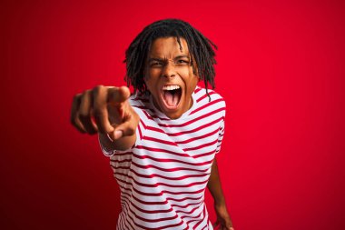 Çizgili t-shirt giyen dreadlocks giyen genç afro adam rahatsız ve kameraya sinirli işaret izole kırmızı arka plan üzerinde duran, kızgın ve öfkeli size