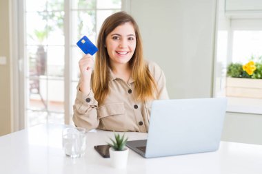 Güzel genç kadın alışveriş online dizüstü bilgisayar ve kredi kartı ile mutlu bir yüz ayakta ve emin bir gülümseme ile diş gösteren gülümseyerek