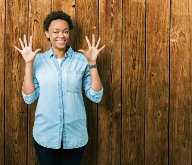 İzole arka plan üzerinde genç güzel Afrikalı Amerikalı kadın gösteren ve parmak numarası on ile işaret kadar güven ve mutlu gülümseyen.