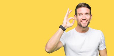 Yakışıklı adam el ve parmaklar ok işaretiyle yapıyor olumlu gülümseyen casual beyaz t-shirt giyiyor. Başarılı ifade.