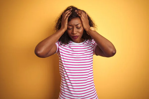 孤立した黄色の背景の上にストライプのTシャツを着た若いアフリカ系アメリカ人女性は 頭痛に苦しんで必死で 痛みと偏頭痛のためにストレスを受けました 頭の上に手を置く — ストック写真