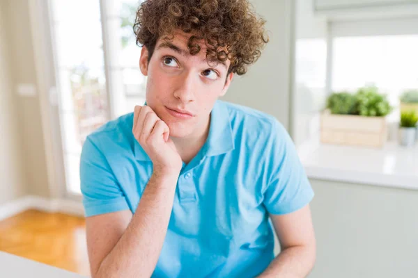 自宅でカジュアルな青いTシャツを着ている若いハンサムな男性は 腕を組んだうつ病の問題に疲れて退屈そうに考えています — ストック写真