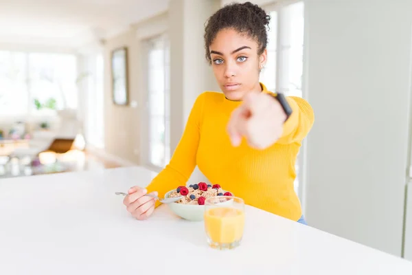 Young african american girl eating healthy cereals for breakfast pointing with finger to the camera and to you, hand sign, positive and confident gesture from the front