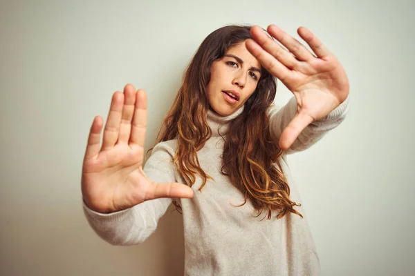 Young beautiful woman wearing winter sweater standing over white isolated background doing frame using hands palms and fingers, camera perspective