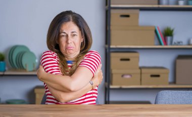 Orta yaş yaşlı kadın yüzünde üzgün ve şok ifade ile kış soğuk için sallayarak ve donma evde masada oturan