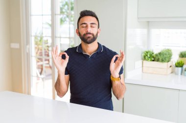 Yakışıklı adam evde sakin ol İspanyol ve gülümseyen gözlerle parmak ile meditasyon jest yapıyor kapalı. Yoga kavramı.