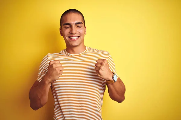 노란색 배경에 줄무늬 티셔츠를 잘생긴 남자는 행복하고 미소를 지으며 성공을 — 스톡 사진