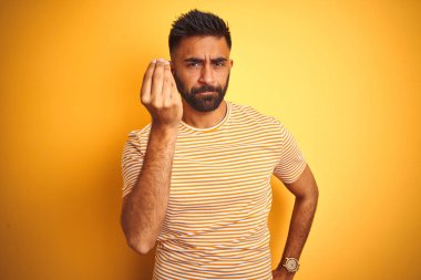 İzole sarı arka plan üzerinde duran t-shirt giyen genç hintli adam el ve parmakları kendinden emin ifade ile İtalyan jest yapıyor