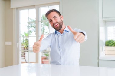 Yakışıklı iş adamı el ile olumlu jest yapıyor onaylayan, başparmak kadar gülümseyerek ve başarı için mutlu. Kameraya bakmak, kazanan jest.