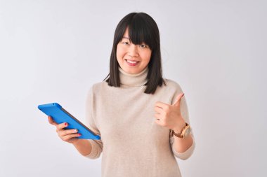 Güzel çinli kadın izole beyaz arka plan üzerinde duran mavi tablet kullanarak büyük bir gülümseme ok işareti yapıyor mutlu, parmakları ile başparmak, mükemmel işareti