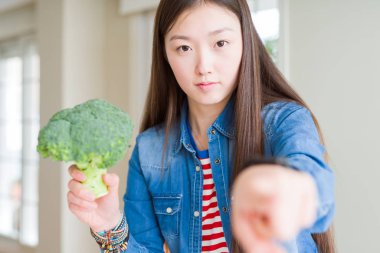 Güzel Asyalı kadın kamera ve size parmak ile işaret Yeşil taze brokoli yeme, el işareti, ön pozitif ve emin jest