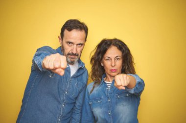Güzel orta yaş çift birlikte izole sarı arka plan yumruk yumruk üzerinde mücadele, agresif ve öfkeli saldırı, tehdit ve şiddet ayakta