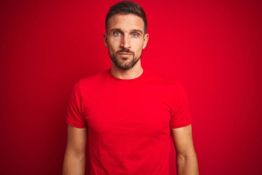 Genç yakışıklı adam kırmızı izole arka plan üzerinde rahat t-shirt giyen yüzünde ciddi ifade ile rahat. Kameraya basit ve doğal bir bakış.