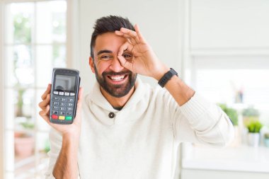 Yakışıklı İspanyol adam mutlu yüz ile satış terminal dataphone tutma noktası parmakları ile bakarak göz el iyle ok işareti yapıyor gülümseyerek