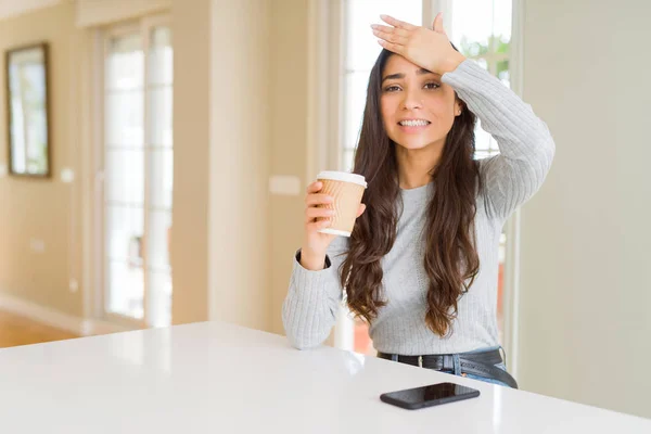 Young woman drinking a cup of coffee at home stressed with hand on head, shocked with shame and surprise face, angry and frustrated. Fear and upset for mistake.