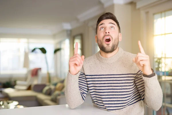 Joven Hombre Guapo Casa Asombrado Sorprendido Mirando Hacia Arriba Señalando —  Fotos de Stock