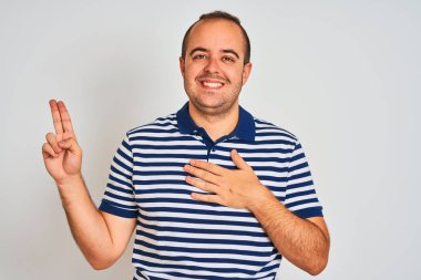 Izole beyaz arka plan üzerinde duran rahat çizgili polo giyen genç adam göğüs ve parmakları üzerinde el ile küfür gülümseyerek, bir sadakat yemini yapma
