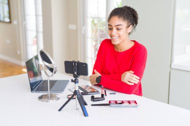 Genç afro-amerikan influencer kadın kayıt yüzünde mutlu ve serin bir gülümseme ile öğretici makyaj. Şanslı kişi.