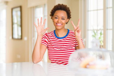 Genç güzel afro-amerikan kadın evde gösteren ve parmakları ile işaret ederken yedi numara kendinden emin ve mutlu gülümseyerek.