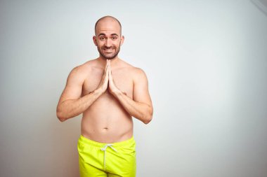 Genç gömleksiz adam izole arka plan üzerinde sarı mayo giyen elleri birlikte emin gülümseyerek af isteyen dua.