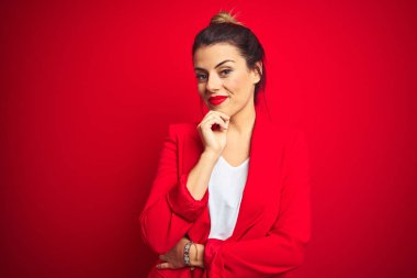 Genç güzel iş kadını kırmızı izole arka plan üzerinde duran kamera güvengörünümlü çapraz kolları ve çene üzerinde kaldırdı el ile gülümseyerek. Olumlu düşünme.